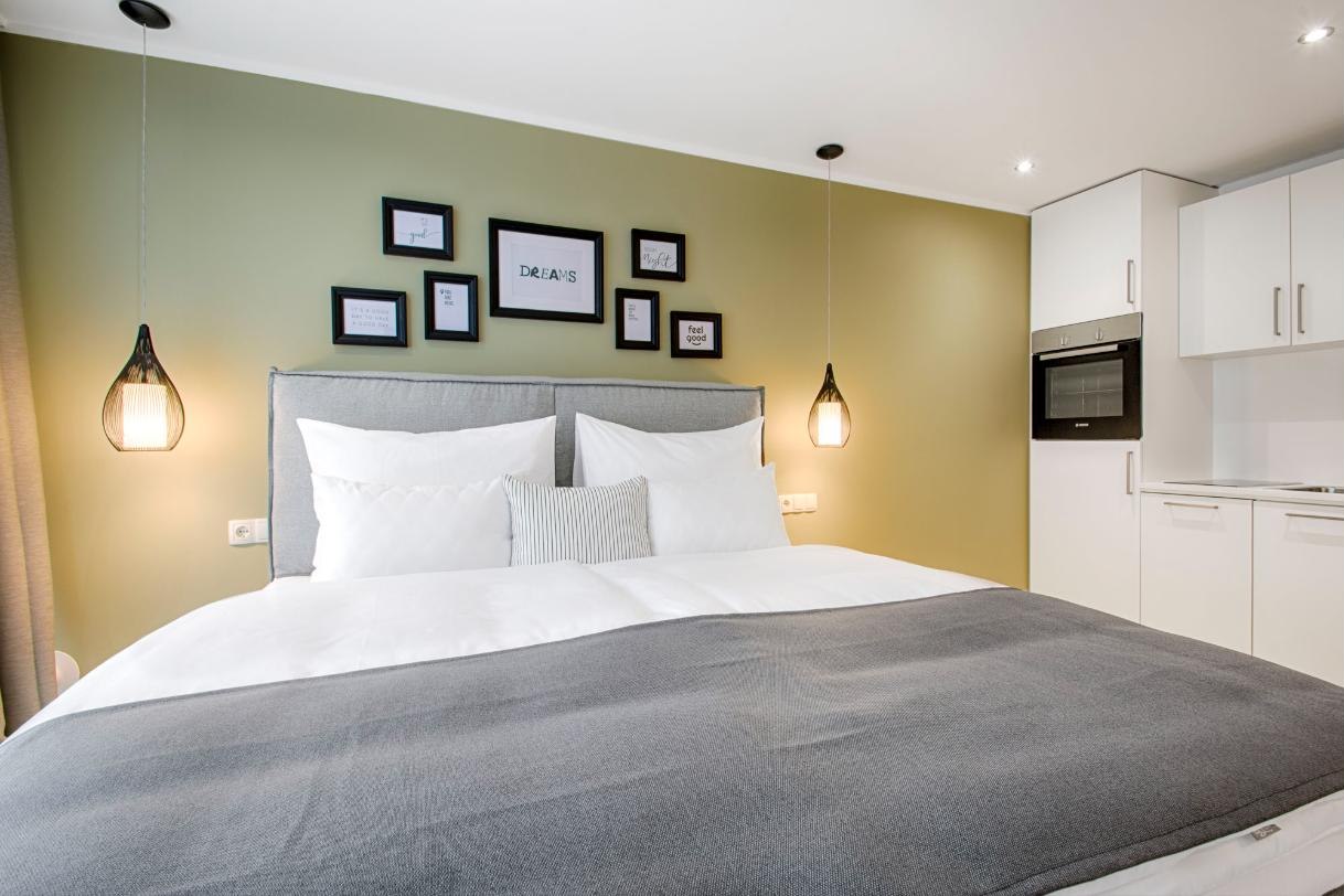 Hotelzimmer mit Doppelbett, grüner Wand mit Bilderrahmen und Pendelleuchten