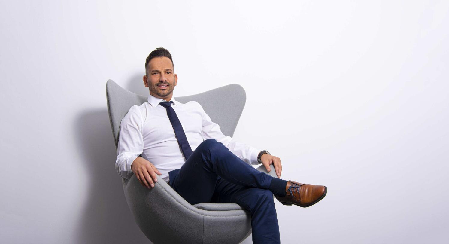 Roberto Maier sitzend in einem grauen Sessel vor heller Wand